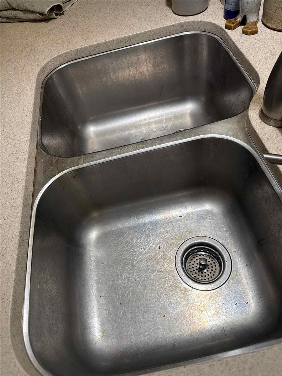 Stainless steel double kitchen sink with water spots and food debris before cleaning in Hopatcong, NJ