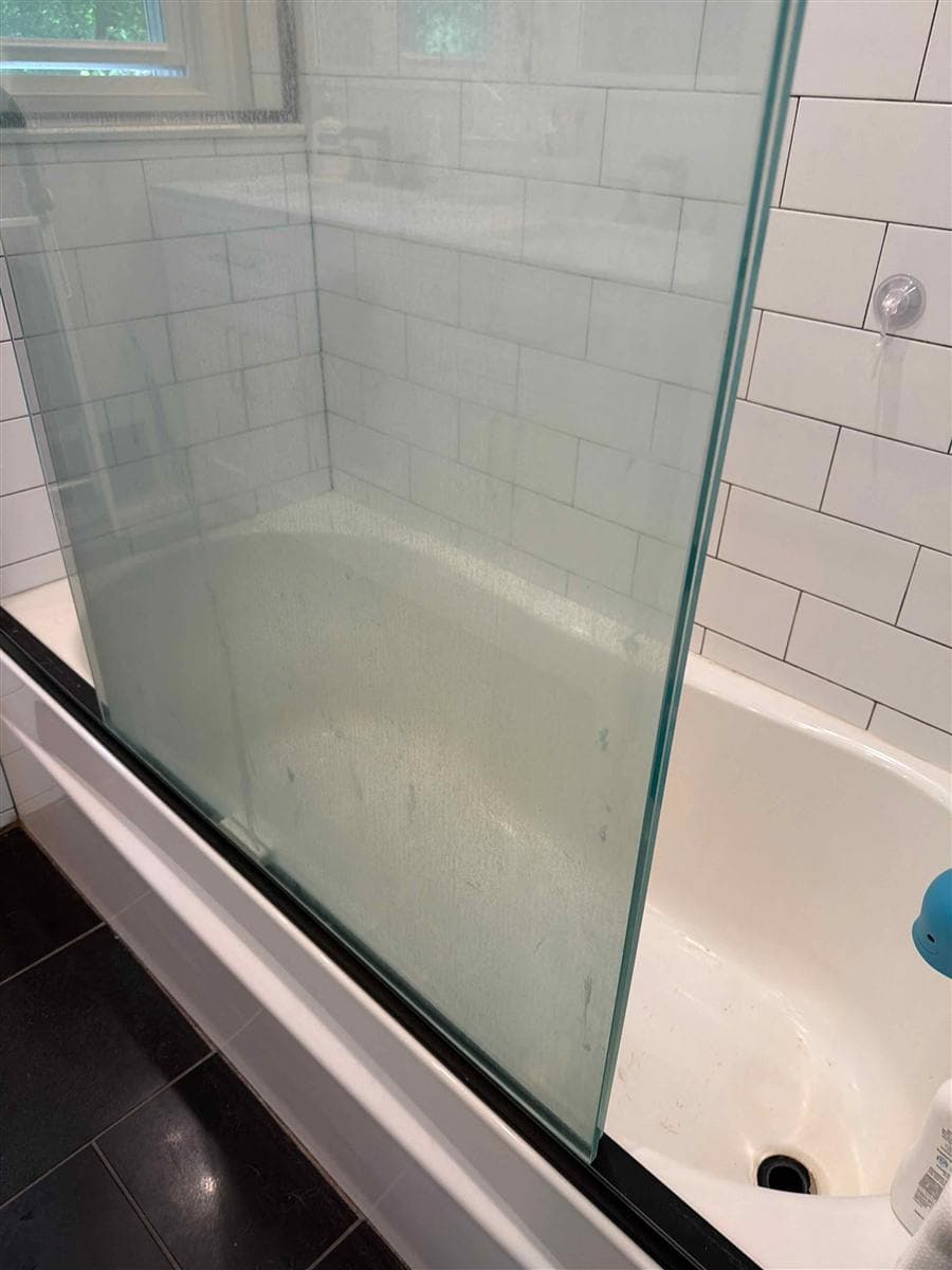 Glass shower door and bathtub covered in hard water spots before cleaning in Rockaway, NJ